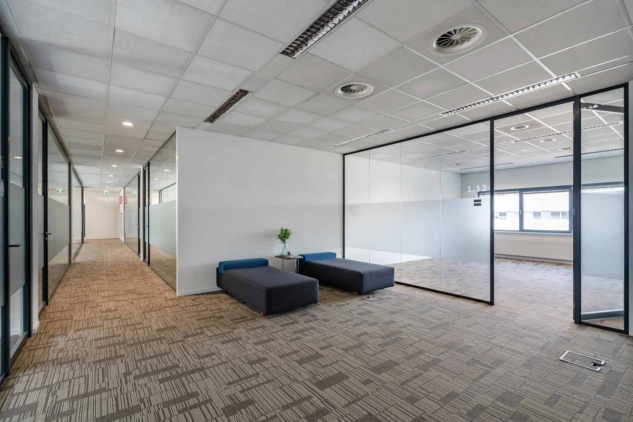 Modern ingericht kantoorinterieur aan het Rivium Boulevard met glazen vergaderruimtes en een wachtruimte met zitbanken.